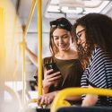 Two women standing together on a bus and looking at a phone